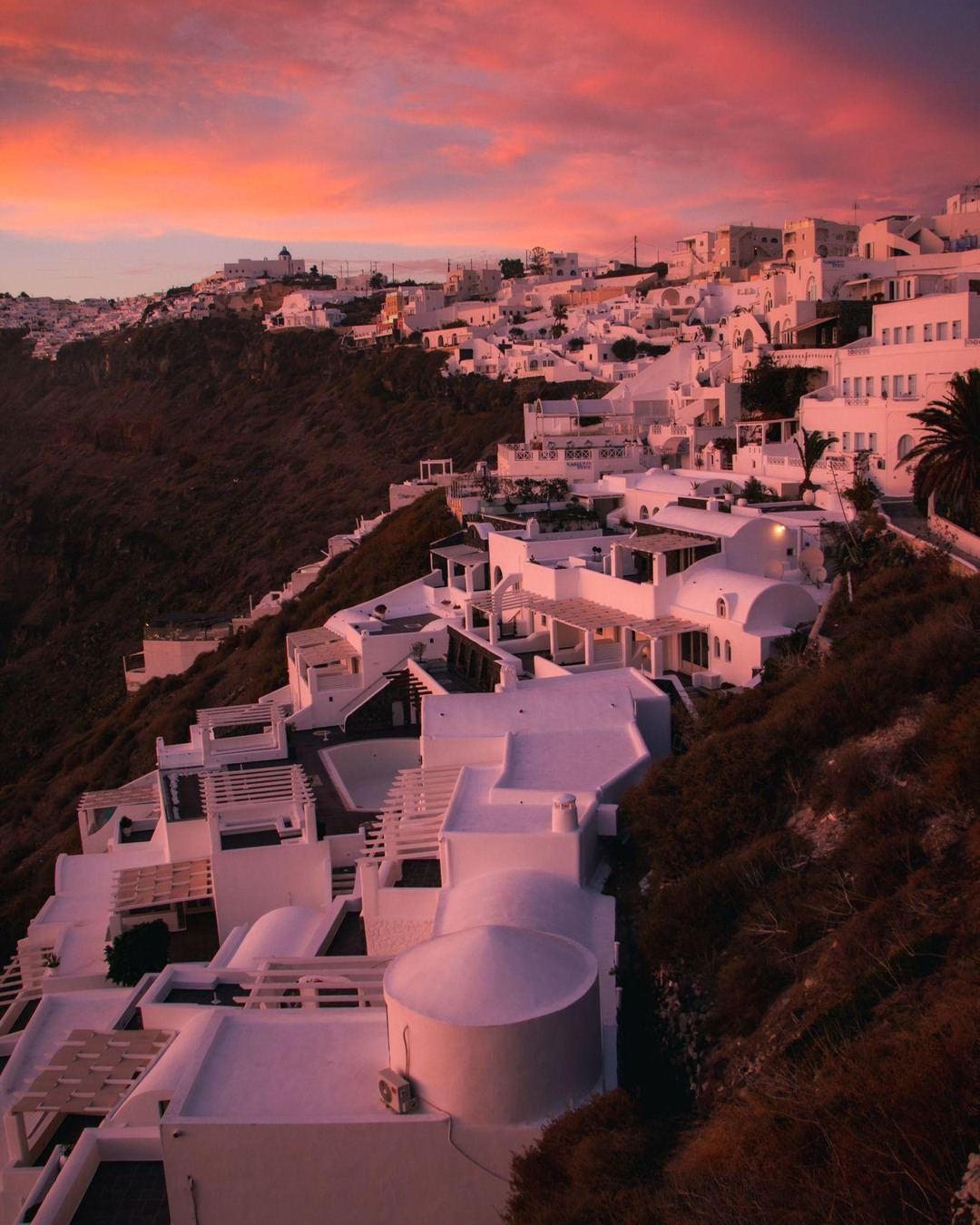 Cliffside terraces glowing pink at dusk in Santorini
