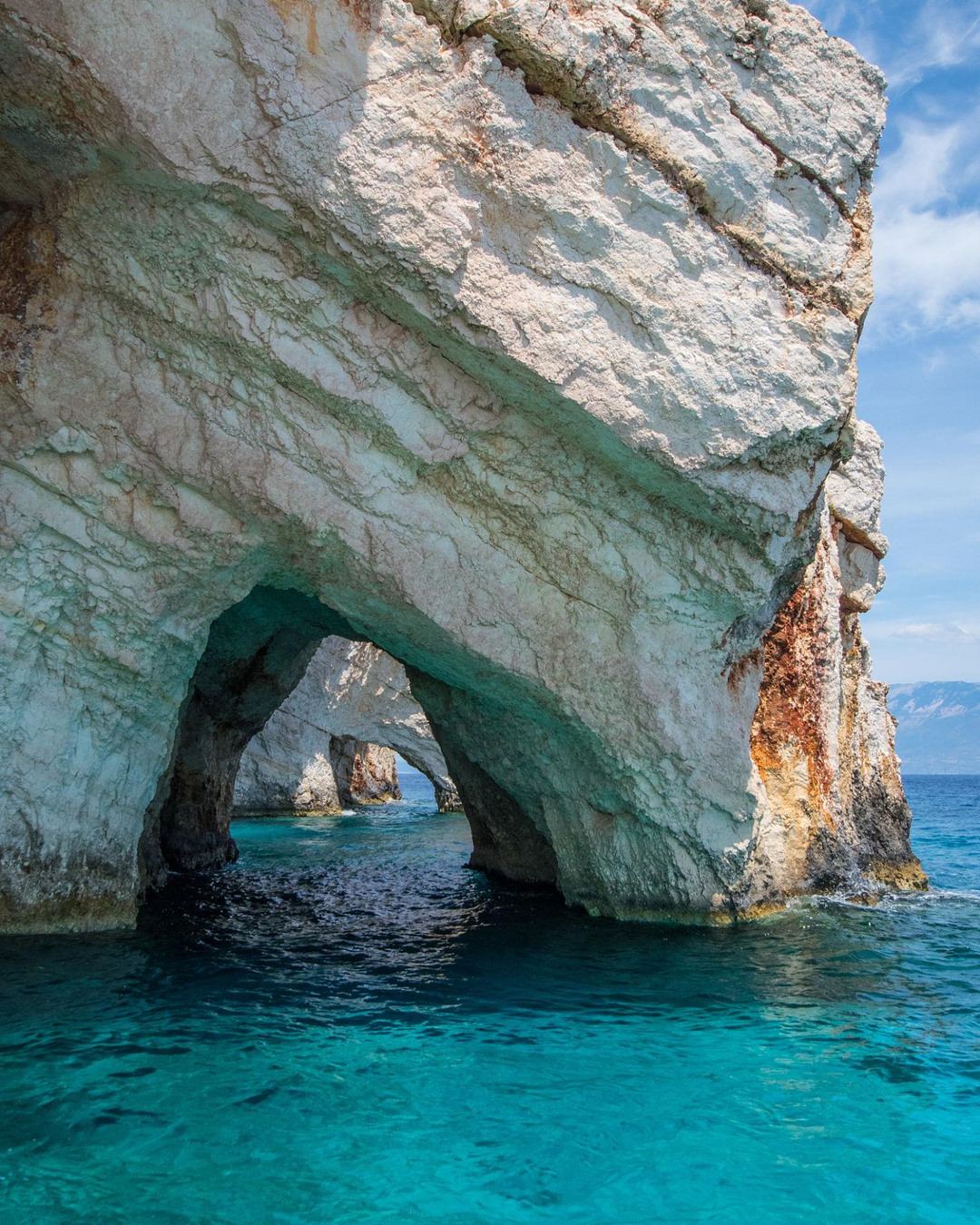 Turquoise water flowing through a sea arch at the Blue Caves of Zante