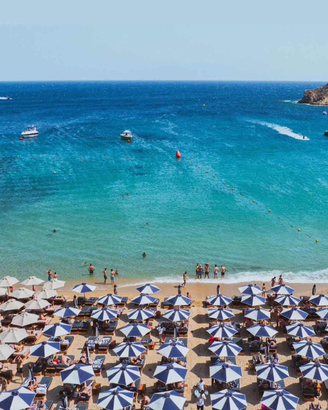 Rows of beach umbrellas on a turquoise Mykonos bay